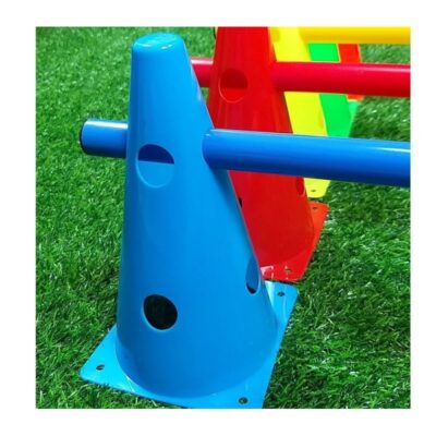 Blue conical climbing toy with holes and a horizontal blue bar, set on green grass with red and yellow parts in the background.