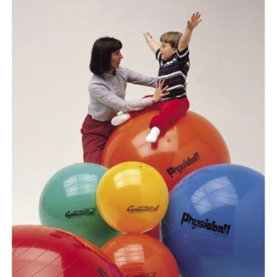 Woman helps a child balance on an orange physio ball surrounded by colorful exercise balls in a therapy/play setting.