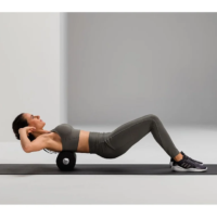 Woman in gray athletic wear lies on a yoga mat with a foam roller under her upper back, performing a thoracic spine stretch.